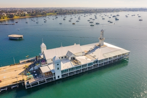 Aerial view of buildings on the end of a pier over a bay with boats anchored in the background - Australian Stock Image