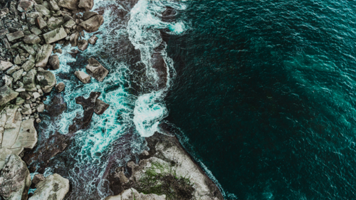 aerial view of clear turquoise water washing over rocky coastline - Australian Stock Image