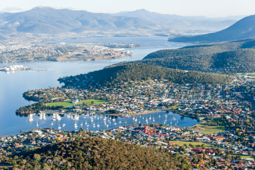 Aerial view of coastal suburb and marina nestled beside forested hills and calm bay - Australian Stock Image