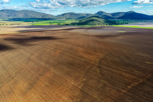 Aerial view of cultivated farmland beneath a dramatic cloudy sky, with a mountain range background - Australian Stock Image
