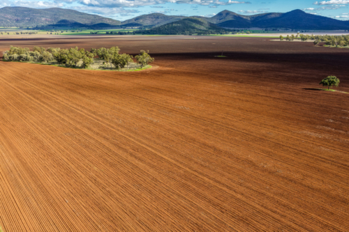 Aerial view of cultivated farmland beneath a dramatic cloudy sky, with a mountain range background. - Australian Stock Image
