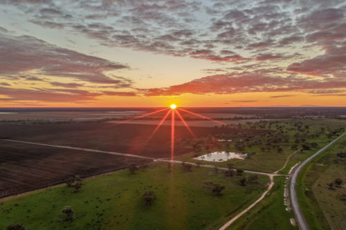 Aerial view of cultivated fields surrounded by a lush green landscape as the rising sun climbs above - Australian Stock Image