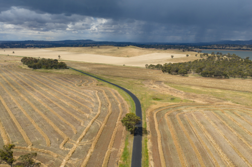 Aerial view of dark clouds and rain over a bend in a country road running through harvested farmland - Australian Stock Image