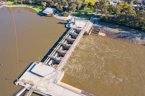 Aerial view of dirty river water rushing through the gates of a weir - Australian Stock Image