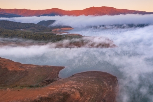 Aerial view of early morning light over a mountain lake covered with fog