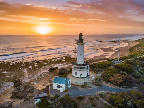 Aerial view of golden sunset over a lighthouse on a coastal cliff - Australian Stock Image