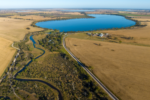 Aerial view of lake surrounded by farmland and rural settlement. - Australian Stock Image