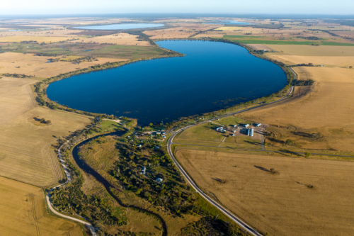 Aerial view of lake surrounded by farmland and rural settlement. - Australian Stock Image