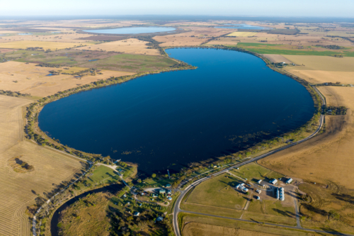 Aerial view of lake surrounded by farmland and rural settlement. - Australian Stock Image