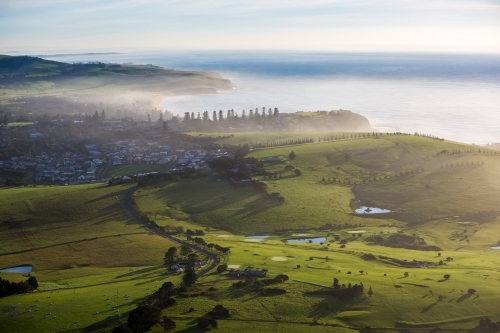 Aerial view of misty rolling hills, golf course and coastal town