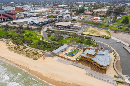 Aerial view of pedestrian bridge over a marina channel cutting through a beach, flowing out to sea - Australian Stock Image