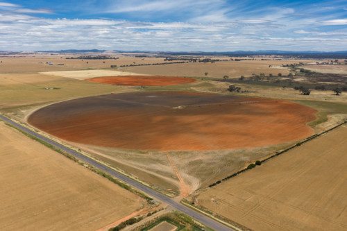 Aerial view of ploughed circular paddock alongside a country road under a blue sky - Australian Stock Image