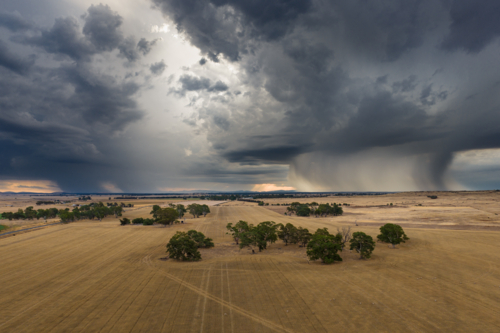 Aerial view of rain falling from dramatic storm clouds over a dry farmland - Australian Stock Image