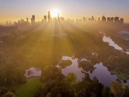 Aerial view of rays of golden sunshine between high rise buildings and over inner city parkland - Australian Stock Image