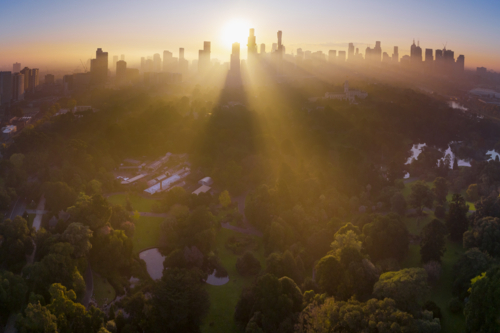 Aerial view of rays of golden sunshine between high rise buildings and over inner city parkland - Australian Stock Image