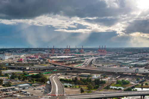 Aerial view of rays of light and rain falling from dark clouds over cranes and freeways in a city - Australian Stock Image