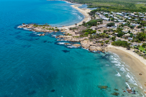 Aerial view of Rose Bay in Bowen, showcasing its shoreline, turquoise waters and rocky headland - Australian Stock Image
