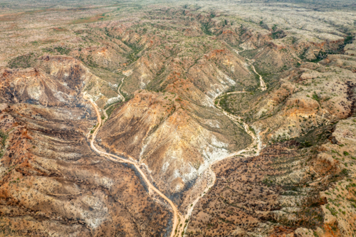 Aerial view of rugged arid gorges and ridges with a winding dirt track through remote ranges - Australian Stock Image