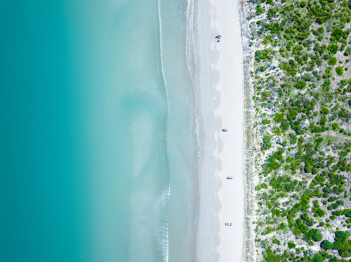 Aerial view of sandy white beach and turquoise ocean water beside coastal vegetation - Australian Stock Image