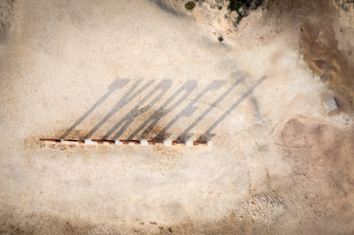 Aerial view of sign casting long shadows across dry ground. - Australian Stock Image