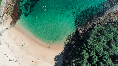 Aerial View of Small Cove Beach with Clear Turquoise Water, swimmers and kayak - Australian Stock Image