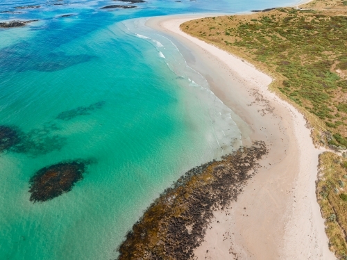 Aerial view of small rocky reefs in turquoise blue water off a white sandy beach - Australian Stock Image