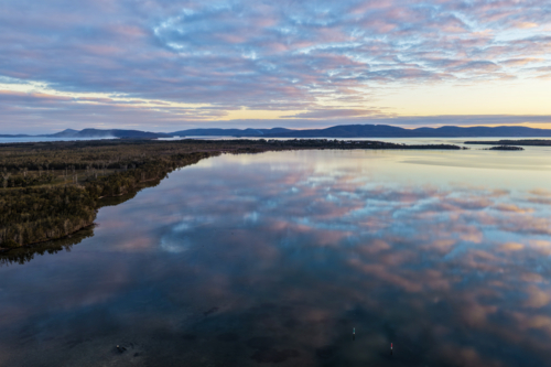 Aerial view of soft pastel clouds reflected across the calm waters of Pipers Bay - Australian Stock Image
