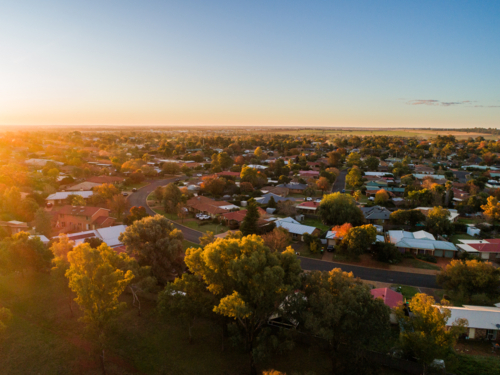 Aerial view of sun on horizon casting warm glow over homes in housing area of Dubbo at sunset  - Australian Stock Image