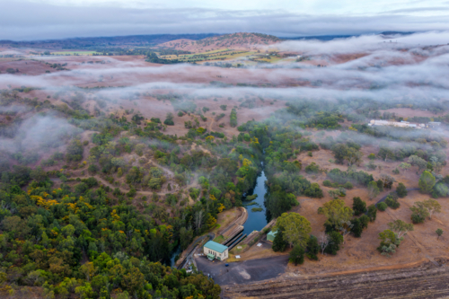 Aerial view of the Glenbawn Dam valve house with fog rolling through the surrounding valley - Australian Stock Image