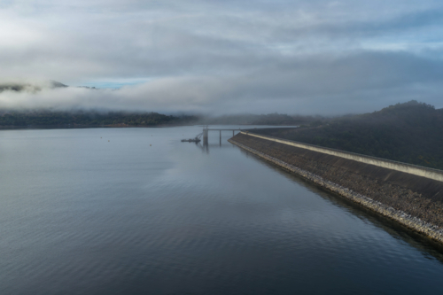 Aerial view of the Glenbawn Dam wall and surrounding landscape with fog rolling through the valley - Australian Stock Image