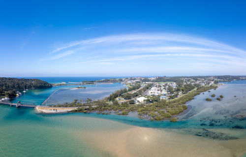 Aerial view of the idyllic coastal town of Narooma at sunset wrapped around the famous Wagonga Inlet - Australian Stock Image
