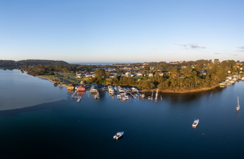 Aerial view of the idyllic coastal town of Narooma at sunset wrapped around the famous Wagonga Inlet - Australian Stock Image