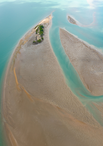 Aerial view of tidal sand flats and green cay amidst clear turquoise sea channels - Australian Stock Image