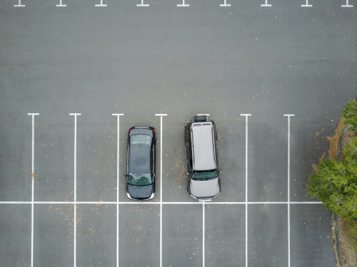 Aerial view of two cars in car park, one of which is over two spaces