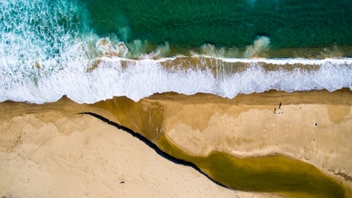 Aerial view of two men surf fishing from the beach as waves crash on the shore