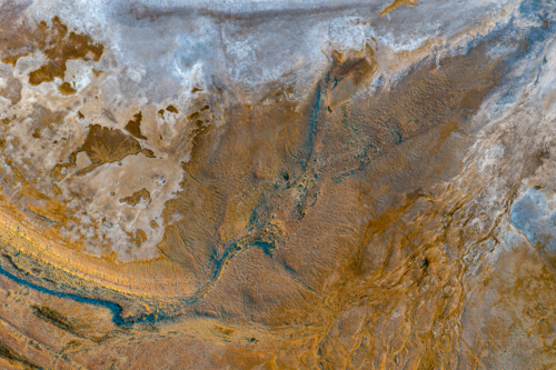 Aerial view of vibrant ochre sediment and deep blue erosion channels on a textured salt pan - Australian Stock Image