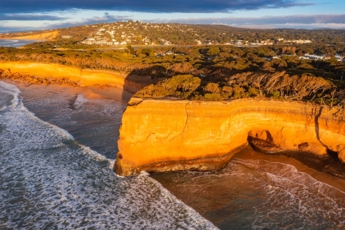 Aerial view of waves breaking against rugged sea cliffs on golden morning sunshine