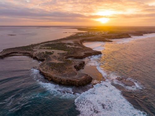 Aerial view of waves crashing against eroded cliffs along a rugged coastline at sunrise - Australian Stock Image