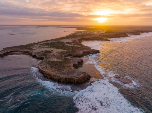 Aerial view of waves crashing against eroded cliffs along a rugged coastline at sunrise