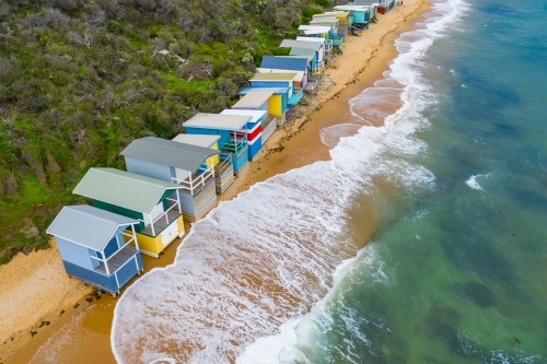 Aerial view of waves crashing on a beach in front of a row of beach huts