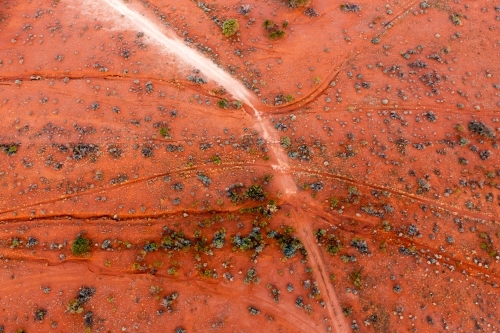 Aerial view of wheel tracks through a dry creek bed in a dry orange outback landscape