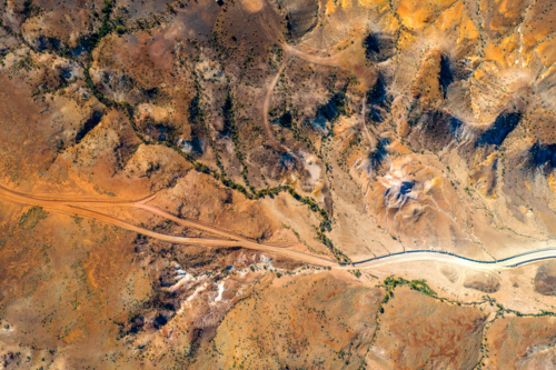 Aerial view of winding desert roads through rugged ochre terrain - Australian Stock Image