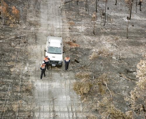 Aerial view of workmen repairing power lines in bushfire ravaged landscape