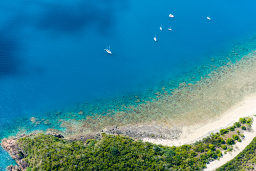 Aerial view of yachts anchored near a coral reef and tropical shoreline - Australian Stock Image