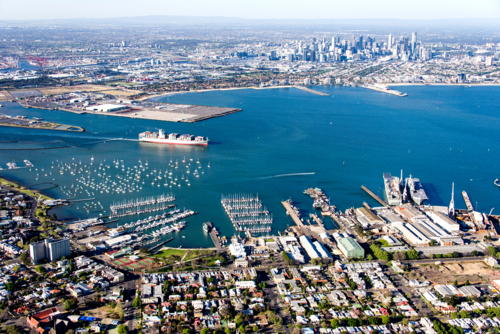 Aerial view over a busy port, city skyline and container ship in harbour - Australian Stock Image