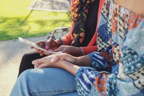 African mother and multicultural teen daughter using mobile phone - Australian Stock Image