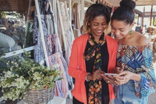 African mother and multicultural teen daughter using mobile phone - Australian Stock Image