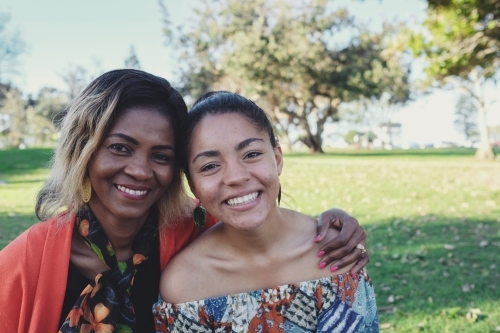 African mother hugging multicultural teen daughter close outdoors - Australian Stock Image