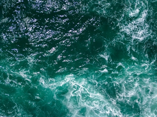 An aerial shot of a turquoise blue waters with white foam patterns on the surface - Australian Stock Image