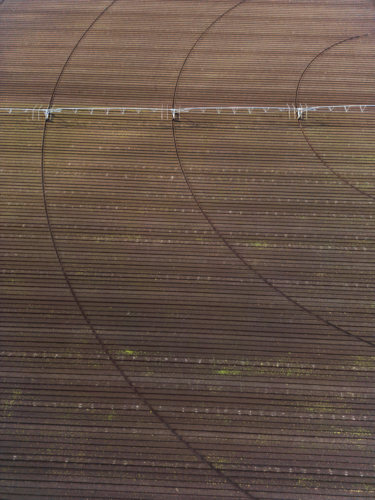 An aerial view of a ploughed deep brown soil field with a centre-pivot irrigator sitting on it - Australian Stock Image
